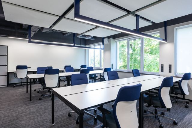 White long tables with comfortable blue armchairs placed in spacious open space office with big window in modern business center